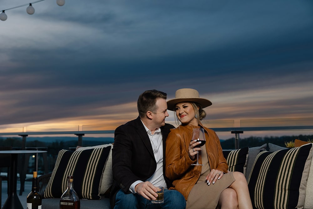 A couple enjoying wine on the outdoor terrace at The Highlander Hotel Radford during sunset, surrounded by cozy seating and a scenic backdrop.